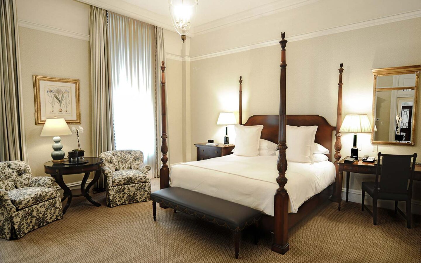 king bed with tall wooden bed posts with a desk and mirror and a small seating area