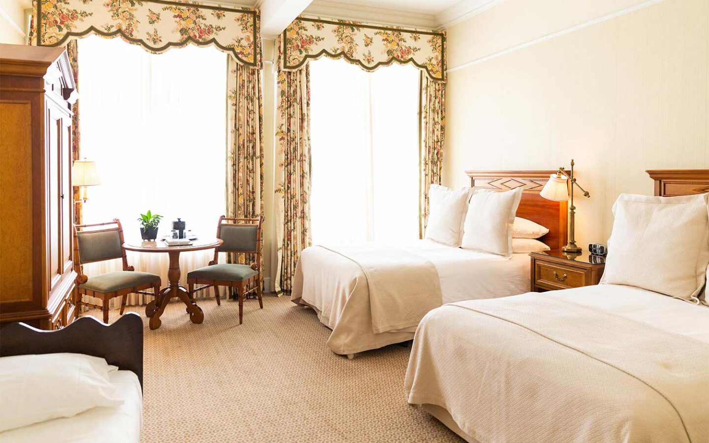 guest room with two double beds, small table, and a large wooden dresser next to two large windows